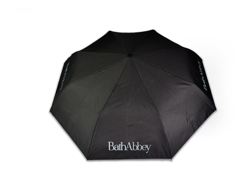 black umbrella open with all black panels displayed with white Bath Abbey text printed on one panel