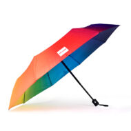 Side view of compact folding umbrella. External panels are printed ombre coral to pink and purple. The inside panels are printed ombre yellow, green, blue through to purple. The pole of the umbrella is black and the handle is black with a silver push button to open and close the umbrella.