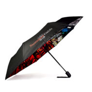 Side open view of folding umbrella. External umbrella panels are black with one panel printed with white and red text that advertises independent school Summer Fields Oxford. The inside of the panels are printed and are a stained glass window in rainbow colours.