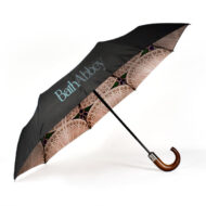 open umbrella on its side with black external panels showing with Bath Abbey text print and underside of umbrella showing with stained glass window print. The umbrella has a dark wooden curve handle