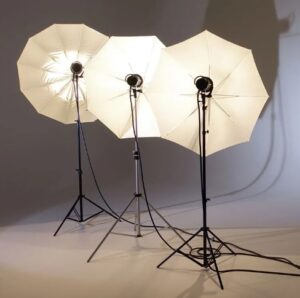 Three umbrellas with lights in on long stands on a white photographer's backdrop